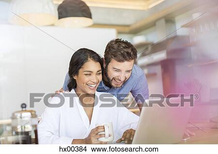 Laughing couple drinking coffee and using laptop View Large Photo Image Picture - Laughing couple drinking coffee and using laptop. Fotosearch