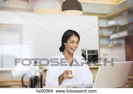 Laughing woman in bathrobe drinking coffee and using laptop View Large Photo Image Picture - Laughing woman in bathrobe drinking coffee and using laptop. Fotosearch