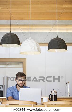 Man using laptop under pendant lights in kitchen View Large Photo Image Picture - Man using laptop under pendant lights in kitchen. Fotosearch