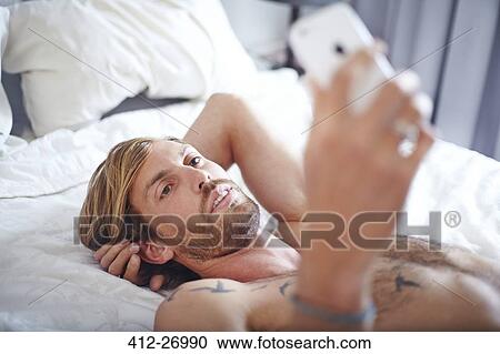 Man with bare chest laying on bed texting with cell phone View Large Photo Image Stock Image - Man with bare chest laying on bed texting with cell phone. Fotosearch