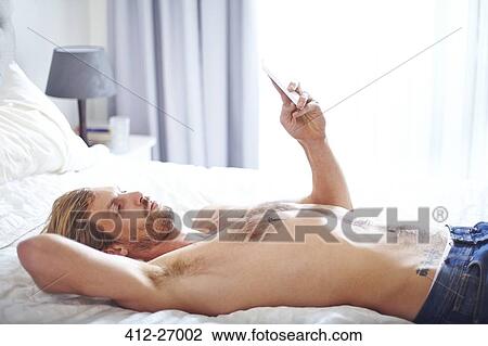 Man with bare chest laying on bed texting with cell phone View Large Photo Image Stock Image - Man with bare chest laying on bed texting with cell phone. Fotosearch