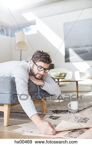 Man with headphones reading newspaper and drinking coffee in living room View Large Photo Image Stock Photo - Man with headphones reading newspaper and drinking coffee in living room. Fotosearch