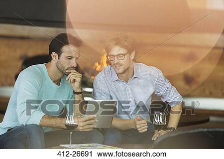 Stock Image - Men drinking red wine and using digital tablet. Fotosearch