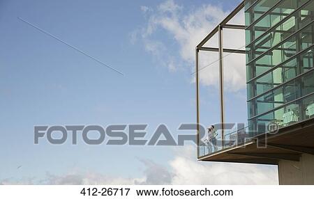 Men standing on balcony of glass bump out against blue sky View Large Photo Image Stock Photo - Men standing on balcony of glass bump out against blue sky. Fotosearch