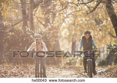 Stock Image - Mother and daughter bike riding on path in woods. Fotosearch