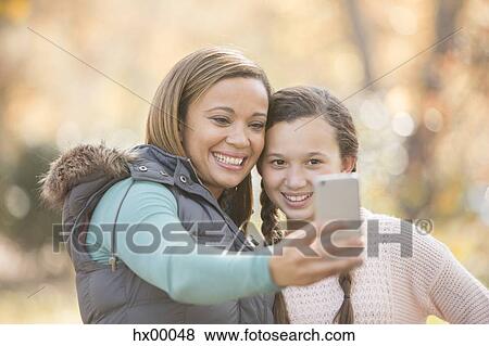 Mother and daughter taking selfie with camera phone outdoors View Large Photo Image Stock Photo - Mother and daughter taking selfie with camera phone outdoors. Fotosearch