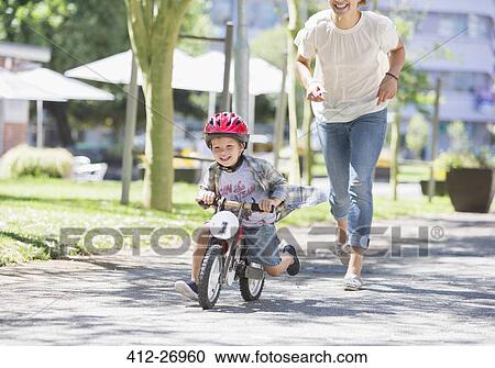 Mother chasing son riding bicycle with helmet in sunny park View Large Photo Image Stock Image - Mother chasing son riding bicycle with helmet in sunny park. Fotosearch