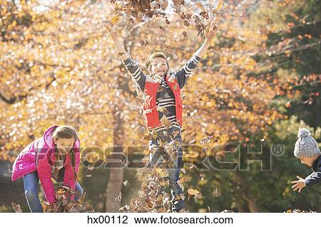 Stock Image - Playful boys and girl running and jumping in autumn leaves. Fotosearch