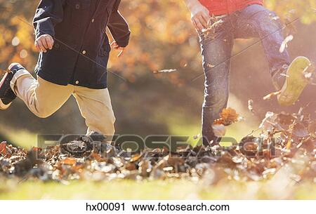Stock Image - Playful boys kicking autumn leaves. Fotosearch