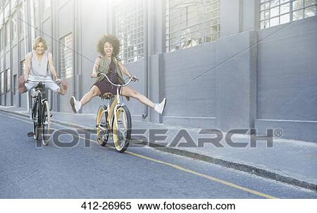 Playful women coasting on bicycles down urban street View Large Photo Image Stock Photography - Playful women coasting on bicycles down urban street. Fotosearch