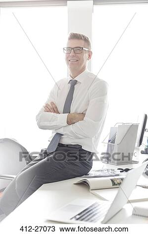 Portrait confident businessman with eyeglasses sitting on desk with arms crossed View Large Photo Image Stock Image - Portrait confident businessman with eyeglasses sitting on desk with arms crossed. Fotosearch