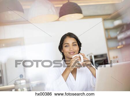 Stock Photograph - Portrait confident woman in bathrobe drinking coffee at laptop. Fotosearch