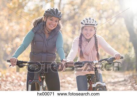Portrait of smiling mother and daughter on mountain bikes in woods View Large Photo Image Stock Image - Portrait of smiling mother and daughter on mountain bikes in woods. Fotosearch