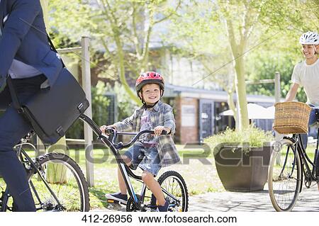 Stock Photograph - Portrait smiling boy in helmet riding tandem bicycle with father in park. Fotosearch