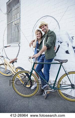 Portrait smiling couple with bicycles hugging at urban wall View Large Photo Image Picture - Portrait smiling couple with bicycles hugging at urban wall. Fotosearch