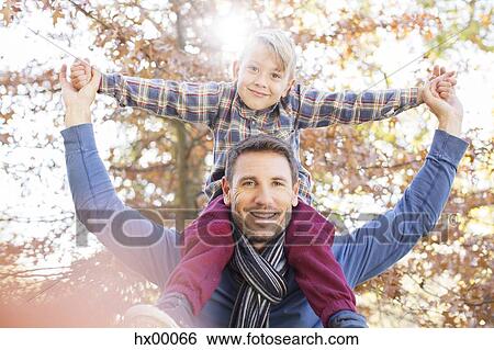 Portrait smiling father carrying son on shoulders below autumn leaves View Large Photo Image Stock Photograph - Portrait smiling father carrying son on shoulders below autumn leaves. Fotosearch