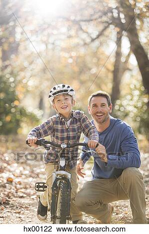 Stock Image - Portrait smiling father teaching son to ride a bike in woods. Fotosearch