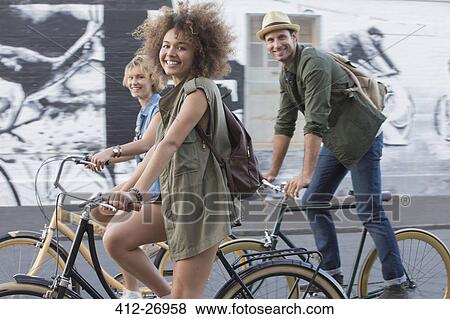 Portrait smiling friends riding bicycles on urban street View Large Photo Image Stock Photo - Portrait smiling friends riding bicycles on urban street. Fotosearch
