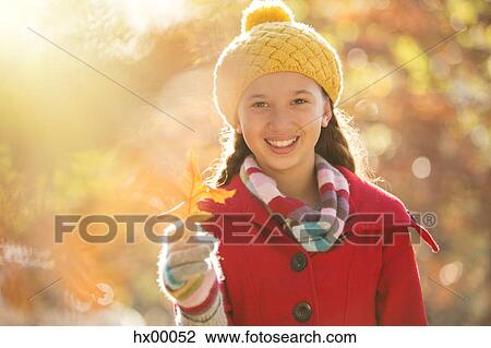 Stock Image - Portrait smiling girl holding golden autumn leaf. Fotosearch