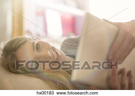 Stock Image - Portrait smiling teenage girl using digital tablet on bed. Fotosearch