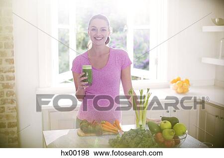 Stock Photo - Portrait smiling woman drinking green smoothie in kitchen. Fotosearch