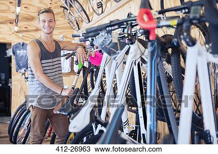 Stock Image - Portrait smiling young man leaning on rack in bicycle shop. Fotosearch