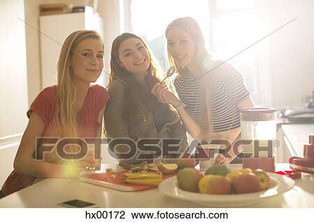 Stock Image - Portrait teenage girls eating in sunny kitchen. Fotosearch