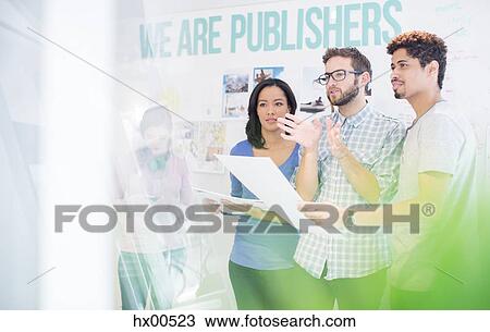 Stock Image - Publishers reviewing and discussing proofs in office. Fotosearch