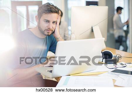 Serious creative businessman using laptop with head in hands in office View Large Photo Image Stock Photo - Serious creative businessman using laptop with head in hands in office. Fotosearch