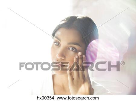 Picture - Serious woman applying moisturizer to face. Fotosearch