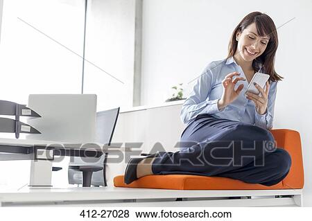 Smiling businesswoman texting with cell phone on cushion in office View Large Photo Image Stock Photo - Smiling businesswoman texting with cell phone on cushion in office. Fotosearch
