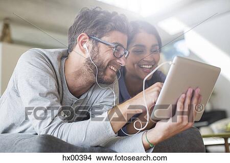 Picture - Smiling couple with headphones using digital tablet. Fotosearch