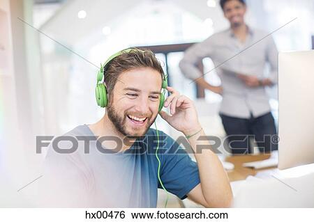 Stock Photograph - Smiling creative businessman listening to headphones in office. Fotosearch