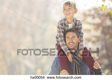 Picture - Smiling father carrying son on shoulders outdoors. Fotosearch