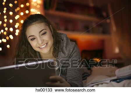 Stock Image - Smiling teenage girl using digital tablet on bed. Fotosearch