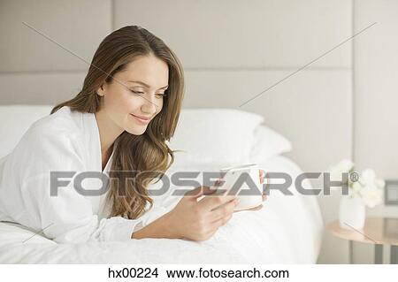 Smiling woman in bathrobe drinking coffee and texting on cell phone on bed View Large Photo Image Picture - Smiling woman in bathrobe drinking coffee and texting on cell phone on bed. Fotosearch
