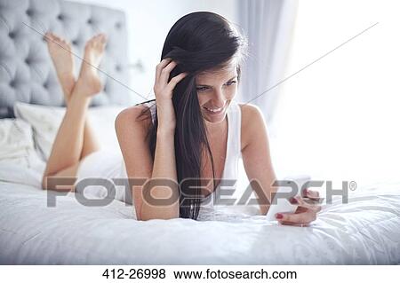 Smiling woman laying on bed texting with cell phone View Large Photo Image Stock Photo - Smiling woman laying on bed texting with cell phone. Fotosearch