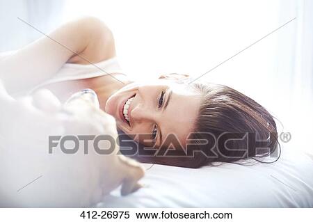 Stock Photography - Smiling woman laying on bed with dog. Fotosearch