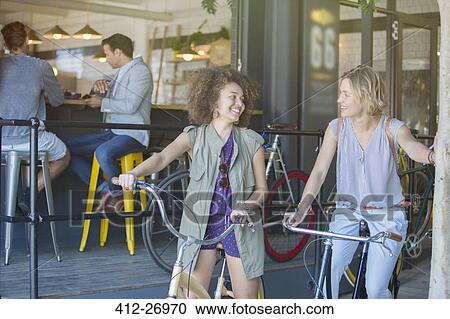Smiling women on bicycles outside cafe patio View Large Photo Image Stock Image - Smiling women on bicycles outside cafe patio. Fotosearch
