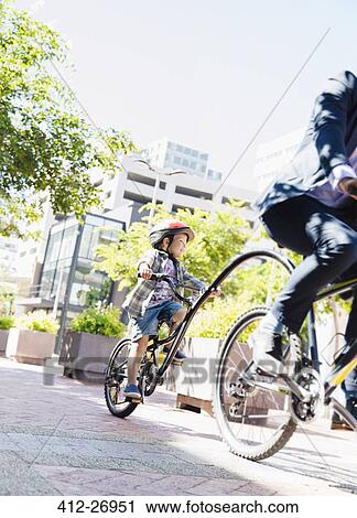 Son in helmet riding tandem bicycle with businessman father in sunny urban park View Large Photo Image Stock Image - Son in helmet riding tandem bicycle with businessman father in sunny urban park. Fotosearch