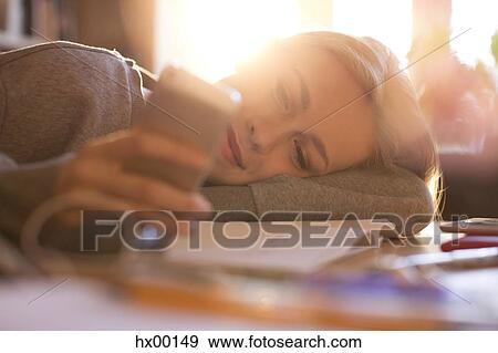 Stock Photo - Teenage girl laying and texting with cell phone. Fotosearch