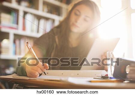 Stock Image - Teenage girl with digital tablet doing homework at sunny desk. Fotosearch