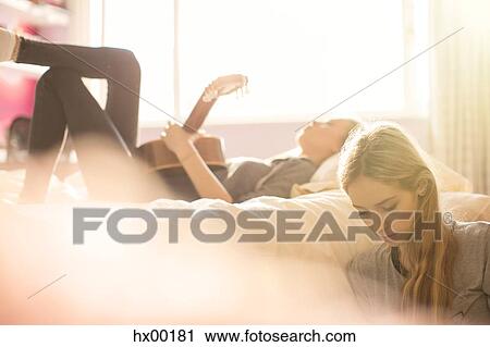 Stock Image - Teenage girls hanging out playing guitar in sunny bedroom. Fotosearch