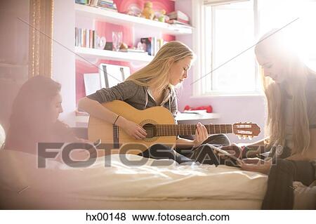 Stock Photo - Teenage girls playing guitar and using digital tablet on bed. Fotosearch