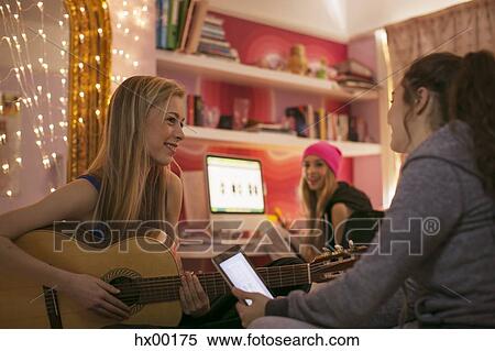 Stock Photography - Teenage girls playing guitar and using digital tablet in bedroom. Fotosearch