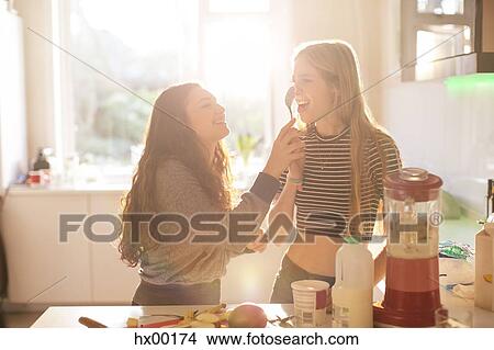 Picture - Teenage girls playing with spoon in sunny kitchen. Fotosearch