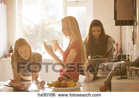 Teenage girls reading magazine, texting and using digital tablet in kitchen View Large Photo Image Stock Photograph - Teenage girls reading magazine, texting and using digital tablet in kitchen. Fotosearch