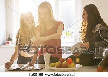 Stock Photo - Teenage girls taking selfie with camera phone in kitchen. Fotosearch