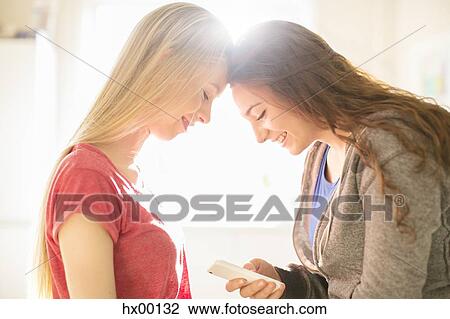 Stock Image - Teenage girls texting with cell phone head to head. Fotosearch
