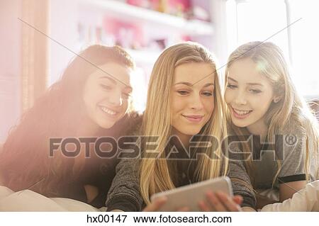 Teenage girls texting with cell phone on bed View Large Photo Image Stock Photo - Teenage girls texting with cell phone on bed. Fotosearch